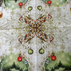 May include: A white Christmas-themed paper napkin with a symmetrical design featuring two angels holding ornaments, a tree, and red and green baubles hanging from branches. The background is a light beige with a snowflake pattern.