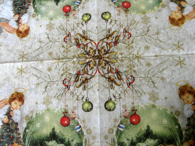May include: A white Christmas-themed paper napkin with a symmetrical design featuring two angels holding ornaments, a tree, and red and green baubles hanging from branches. The background is a light beige with a snowflake pattern.