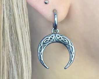 May include: A silver ear cuff and a silver crescent moon dangle earring with a Celtic knot design.