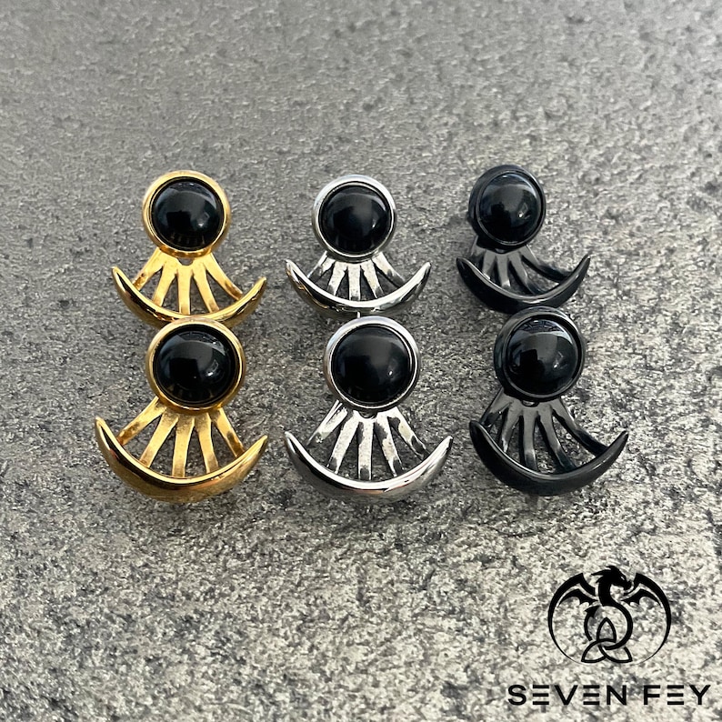 Puede incluir: Tres pares de pendientes con detalles de piedras preciosas negras. Los pendientes est&aacute;n hechos de metal dorado, plateado y negro. Cada pendiente presenta un dise&ntilde;o de media luna con un patr&oacute;n de rayos de sol.