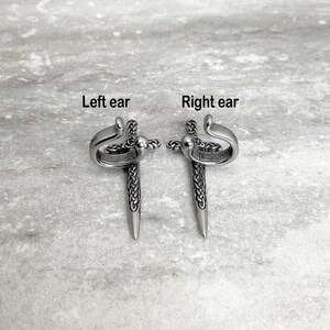 May include: A pair of silver ear cuffs in the shape of a sword with a Celtic knot design. The cuffs are labeled "Left ear" and "Right ear".