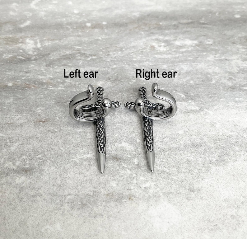 May include: A pair of silver ear cuffs in the shape of a sword with a Celtic knot design. The cuffs are labeled "Left ear" and "Right ear".