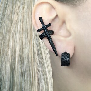 May include: A black sword ear cuff and a black hoop earring with a Celtic knot design.