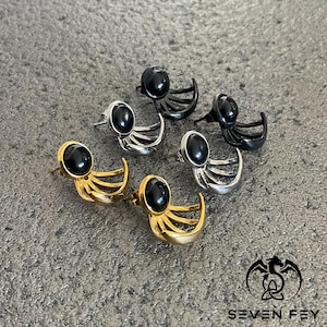 Puede incluir: Cuatro pares de pendientes con detalles de piedras preciosas negras. Cada par presenta un dise&ntilde;o de luna creciente con tres l&iacute;neas curvas que se extienden desde la luna. Los pendientes est&aacute;n disponibles en oro, plata y negro.