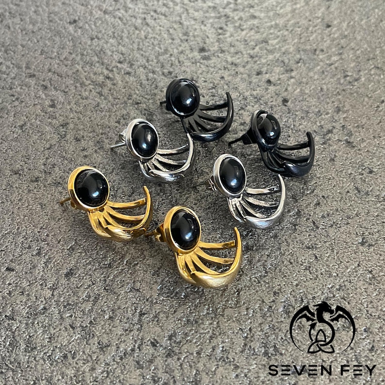 Puede incluir: Cuatro pares de pendientes con detalles de piedras preciosas negras. Cada par presenta un dise&ntilde;o de luna creciente con tres l&iacute;neas curvas que se extienden desde la luna. Los pendientes est&aacute;n disponibles en oro, plata y negro.