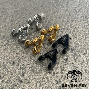 May include: Three pairs of earrings in the shape of a claw, one pair is gold, one pair is silver, and one pair is black.