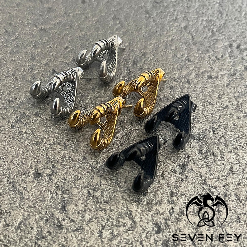 May include: Three pairs of earrings in the shape of a claw, one pair is gold, one pair is silver, and one pair is black.