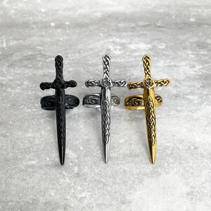 May include: Three sword rings, one black, one silver, and one gold. Each ring features a detailed sword design with a Celtic knot pattern.