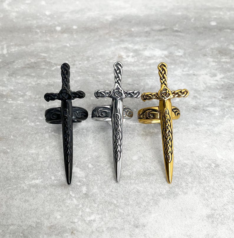 May include: Three sword rings, one black, one silver, and one gold. Each ring features a detailed sword design with a Celtic knot pattern.