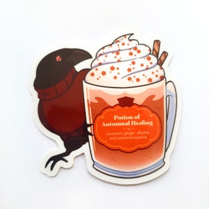May include: A sticker featuring a cartoon raven holding a mug of orange-colored liquid topped with whipped cream and sprinkles. The mug has a label that reads "Potion of Autumnal Healing, cinnamon, ginger, allspice, and autumnal essence."