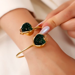 Puede incluir: Un brazalete de oro con dos abalorios en forma de granada verde. Los abalorios est&aacute;n llenos de cuentas verdes.