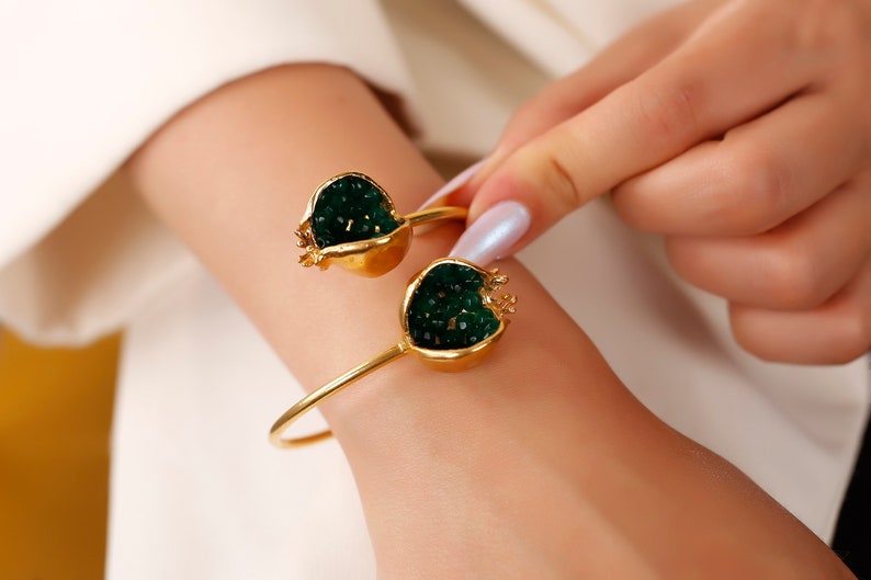 Puede incluir: Un brazalete de oro con dos abalorios en forma de granada verde. Los abalorios est&aacute;n llenos de cuentas verdes.