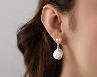 May include: A pair of silver earrings with a small, round, golden pearl and a larger, irregular, white pearl dangling from it.