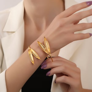 May include: Gold leaf-shaped bracelet with a delicate design. The bracelet is open and adjustable to fit different wrist sizes.