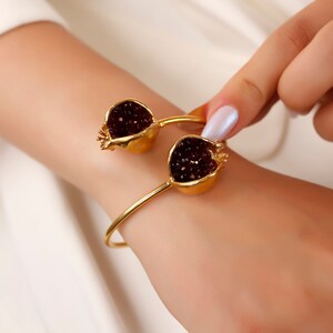Puede incluir: Una pulsera de oro con dos abalorios en forma de granada. Los abalorios est&aacute;n llenos de cristales rojo oscuro.