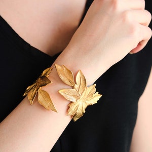 May include: A gold leaf bracelet with a delicate design. The bracelet is made of metal and features a series of leaves that are connected together.