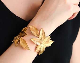 Puede incluir: Un brazalete de hojas de oro con un diseño delicado. El brazalete está hecho de metal y presenta una serie de hojas que están conectadas entre sí.
