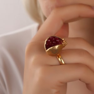 Può includere: Un anello d'oro a forma di melograno con pietre rosse simili a rubini all'interno.