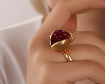May include: A gold ring shaped like a pomegranate with red ruby-like stones inside.