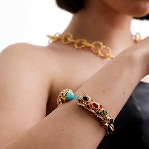 May include: A gold bangle bracelet with colourful oval-shaped gemstones. The bracelet is open and has a hinge on one side.