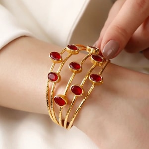 May include: Gold bangle bracelet with multiple bands and red gemstone accents.
