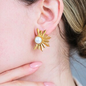 May include: Gold earrings with a pearl in the center and a sunburst design.