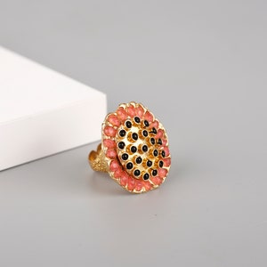 May include: A gold ring with a large, round, black and pink design. The ring is decorated with small, round black stones and pink beads.