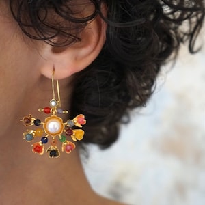 Puede incluir: Pendientes de oro con un centro de perla y piedras de colores en forma de flores.
