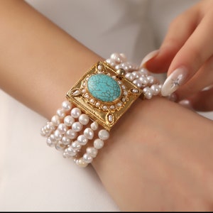May include: A gold bracelet with a turquoise stone set in a square frame. The bracelet is made of multiple strands of white pearls.
