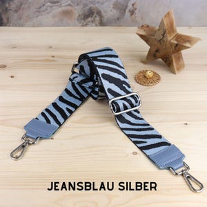 Könnte beinhalten: Ein verstellbarer Gurt mit silberner Beschläge, mit einem blauen und schwarzen Zebra-Muster. Der Gurt ist aus Stoff und hat ein gewebtes Design. Der Gurt heißt "Jeansblau Silber".