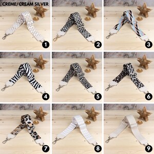 May include: Nine different patterned and solid color adjustable straps for bags. The straps are made of a woven fabric and have a silver metal buckle. The straps are displayed on a wooden surface with a star-shaped decoration.