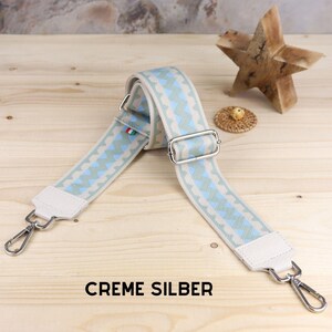 May include: A beige and light blue patterned adjustable strap with silver hardware and the text "CREME SILBER".