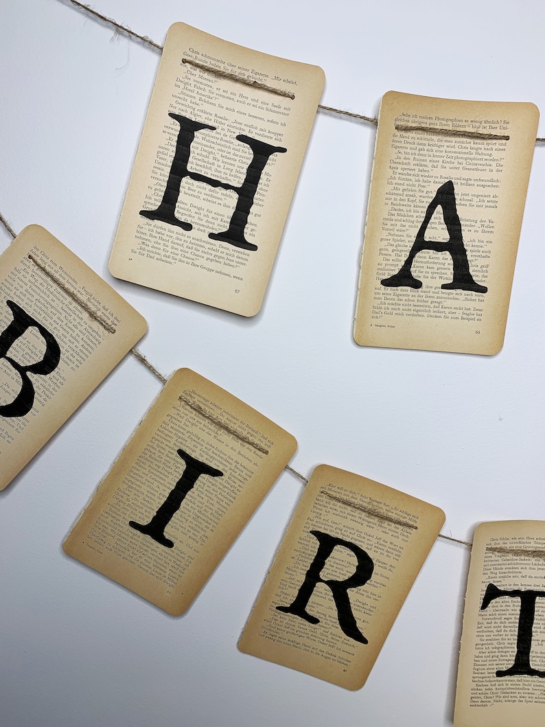 Pu&ograve; includere: Uno striscione fatto di vecchie pagine di libri con la parola "HAPPY BIRTHDAY" stampata in lettere nere. Lo striscione &egrave; legato insieme con uno spago.