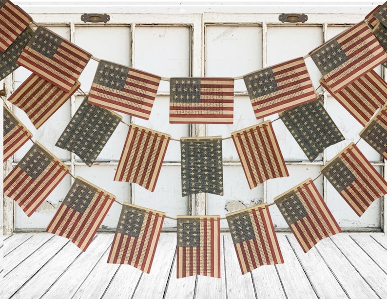 May include: A decorative bunting garland featuring multiple rectangular flags printed with the United States flag design. The flags are arranged in two cascading rows, suspended by a thin cord, and display a weathered, textured appearance.