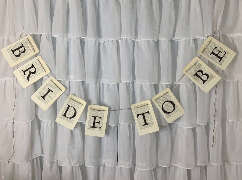 Pu&ograve; includere: Uno sfondo in tessuto bianco con uno striscione che recita "Bride to Be" in lettere nere su sfondo bianco. Lo striscione &egrave; composto da singole carte con ogni lettera stampata su una carta separata.
