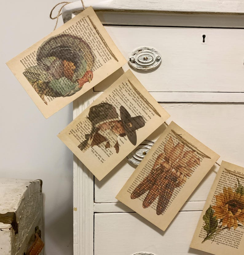 May include: Thanksgiving-themed banner featuring illustrations of a turkey, pilgrim, corn, and sunflower. Each image is printed on a page from a vintage book, creating a rustic and charming aesthetic. The banner is strung together with twine.