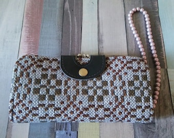 May include: A gray and brown woven clutch purse with a black leather flap and a gold clasp. The purse has a pink beaded strap.