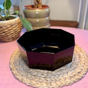 Peut inclure: Un bol octogonal noir brillant avec une large ouverture et des parois droites et inclinées. Le bol présente une surface lisse et réfléchissante ainsi qu'un intérieur profond, mettant en valeur une forme géométrique au design épuré.