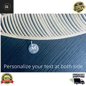 May include: A small, round silver pendant with the letter "M" engraved on it, suspended against a dark blue surface. The pendant is attached to a delicate chain. The text "Personalize your text at both side" is visible.