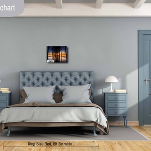 May include: A bedroom interior design mockup featuring a king-size bed with a blue headboard and a gray wall. A framed photograph of a sunset over a pier is hanging above the bed. The bed is 6 feet 3 inches wide and the photo is 16 inches by 20 inches.