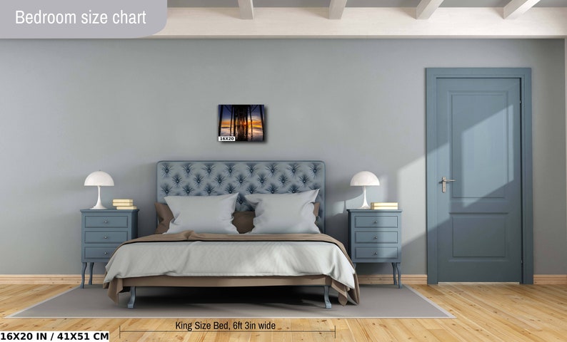 May include: A bedroom interior design mockup featuring a king-size bed with a blue headboard and a gray wall. A framed photograph of a sunset over a pier is hanging above the bed. The bed is 6 feet 3 inches wide and the photo is 16 inches by 20 inches.