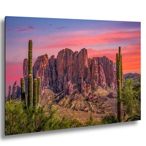 May include: A vibrant landscape print featuring a desert scene with towering cacti and a majestic mountain range. The sky is ablaze with pink and orange hues, creating a dramatic sunset backdrop. Green foliage and desert plants are in the foreground.