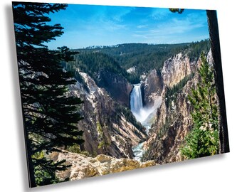 May include: A panoramic view of a waterfall cascading down a rocky canyon in a lush green forest. The water is white and foamy, and the sky is blue with white clouds.