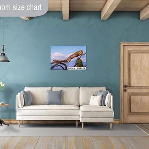 May include: A framed canvas print of a bird perched on a branch, set against a blue sky with clouds. The print is labeled with dimensions of 24x36 inches / 61x91 cm. The artwork hangs above a cream-colored sofa.