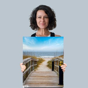 May include: A wooden walkway leads to a sandy beach with blue water and a clear sky. The walkway is lined with tall grass on either side. The image is labelled "16x20".