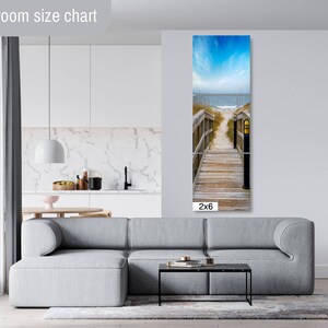 May include: A photograph of a wooden walkway leading to the beach. The walkway is lined with wooden railings and has a lamp post at the end. The beach is in the background and the sky is blue with white clouds. The image is labelled "2x6".
