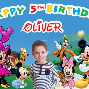 May include: A birthday banner with the words "Happy 5th Birthday Oliver" in colorful letters. The banner features Mickey Mouse, Minnie Mouse, Goofy, and Pluto. There are also balloons in the background.