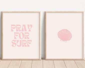 May include: Two framed prints with a pink background. The left print features the text "Pray for Surf" in a pink retro font. The right print features a pink seashell.