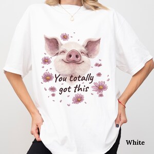 May include: White t-shirt featuring a smiling pig illustration with pink flowers. The text "You totally got this" is printed below the pig. The shirt is a casual, oversized fit.