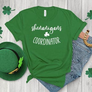 Peut inclure: T-shirt vert avec un texte blanc qui dit "Shenanigans Coordinator" et un graphique de tr&egrave;fle.